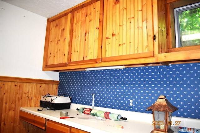 kitchen featuring brown cabinets, a wainscoted wall, light countertops, and wood walls