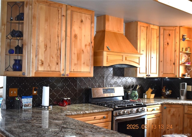 kitchen featuring premium range hood, dark stone counters, tasteful backsplash, and stainless steel range with gas stovetop