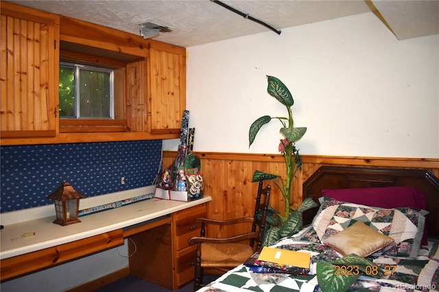 bedroom with wooden walls, wainscoting, a textured ceiling, and built in study area