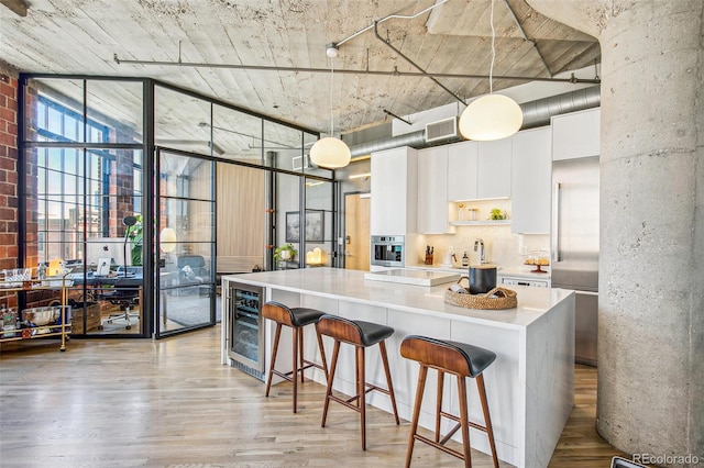 kitchen featuring light wood-type flooring, white cabinetry, beverage cooler, and decorative light fixtures