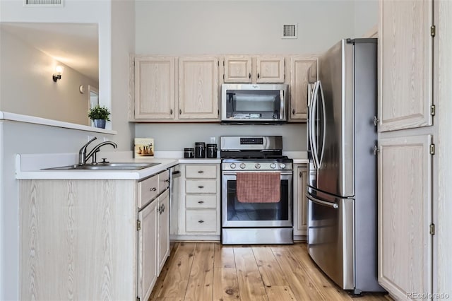 kitchen with stainless steel appliances, a sink, light countertops, light wood-style floors, and light brown cabinetry
