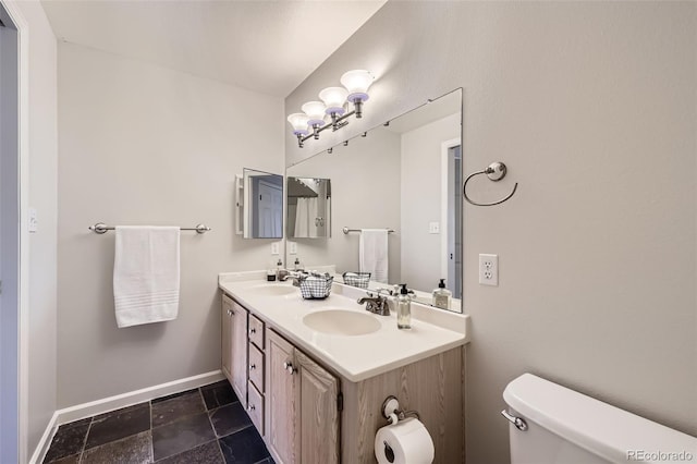 bathroom featuring baseboards, toilet, double vanity, and stone finish floors