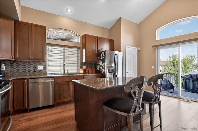 18153 E Amherst Dr, Aurora, CO 80013 - kitchen featuring appliances with stainless steel finishes, a kitchen breakfast bar, light wood-type flooring, tasteful backsplash, and a high ceiling