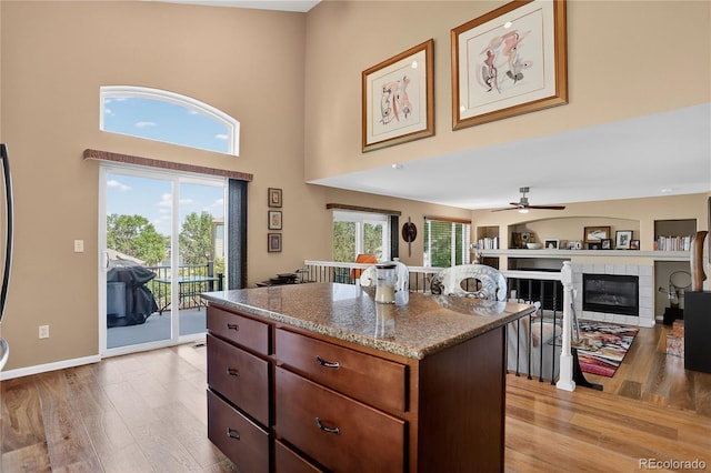 18153 E Amherst Dr, Aurora, CO 80013 - kitchen featuring light wood-style flooring, a center island, a fireplace, a high ceiling, and a ceiling fan