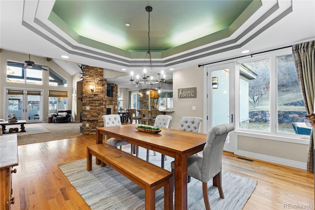 dining area featuring ceiling fan with notable chandelier, light hardwood / wood-style flooring, ornate columns, and a raised ceiling