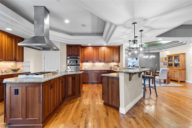 kitchen with a spacious island, island range hood, hanging light fixtures, and a raised ceiling