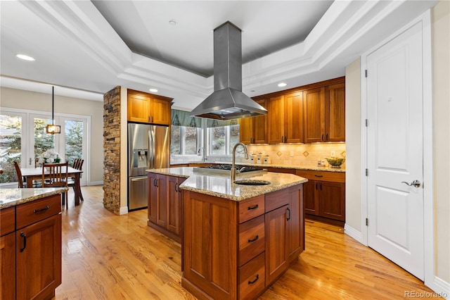 kitchen featuring stainless steel appliances, a tray ceiling, island exhaust hood, and a kitchen island with sink