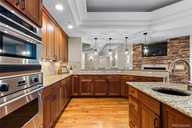 kitchen featuring light stone countertops, decorative backsplash, pendant lighting, sink, and kitchen peninsula