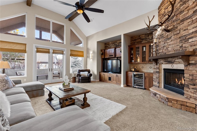 living room with wine cooler, a stone fireplace, bar area, light carpet, and high vaulted ceiling