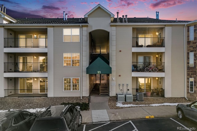 back of property at dusk featuring central AC unit and uncovered parking