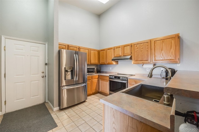 kitchen featuring under cabinet range hood, light tile patterned floors, a high ceiling, stainless steel appliances, and a sink