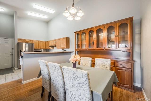 dining space featuring an inviting chandelier, light wood-style floors, baseboards, and high vaulted ceiling