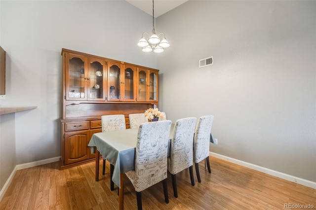 dining room featuring light wood-type flooring, visible vents, an inviting chandelier, baseboards, and a towering ceiling