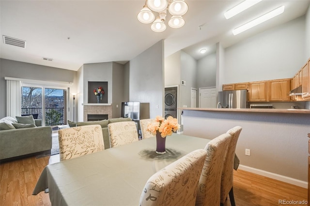 dining space with visible vents, wood finished floors, a tile fireplace, and stacked washing maching and dryer