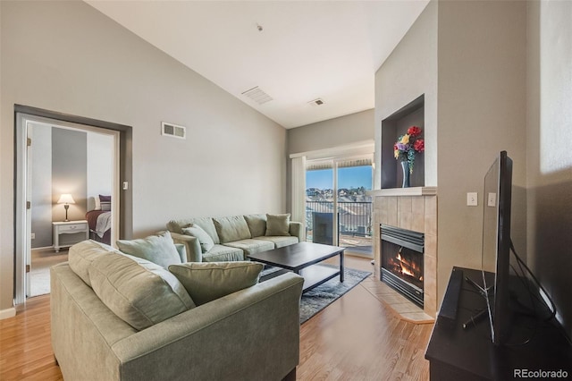 living area featuring visible vents, light wood-style flooring, a fireplace, and vaulted ceiling