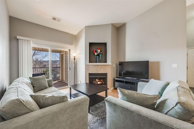 living area featuring a tiled fireplace, vaulted ceiling, visible vents, and wood finished floors