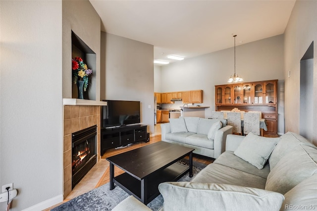 living area with light tile patterned floors, a tile fireplace, a high ceiling, and baseboards