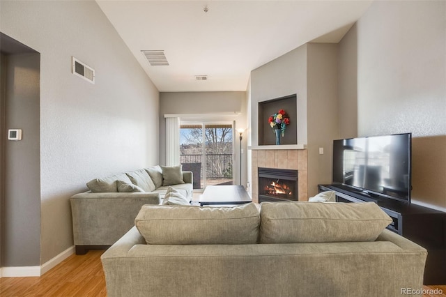 living area featuring a tiled fireplace, baseboards, visible vents, and light wood-type flooring