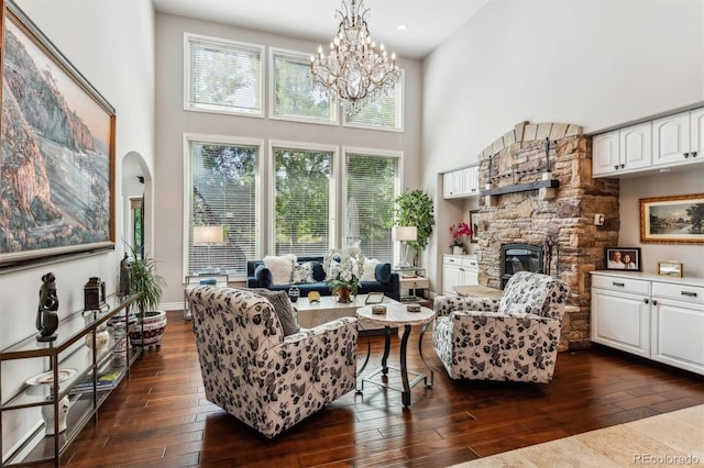 living room featuring a high ceiling, a stone fireplace, dark hardwood / wood-style floors, and a chandelier