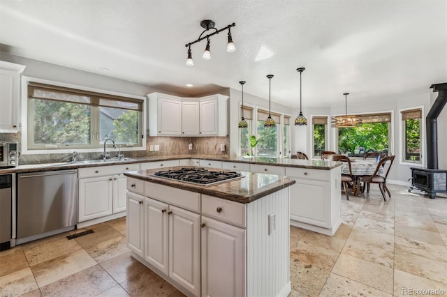 kitchen featuring sink, a wood stove, white cabinetry, appliances with stainless steel finishes, and a center island