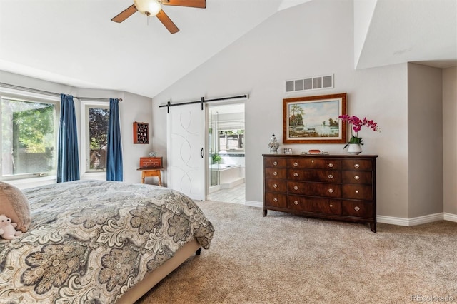 bedroom with vaulted ceiling, a barn door, ceiling fan, ensuite bathroom, and light carpet