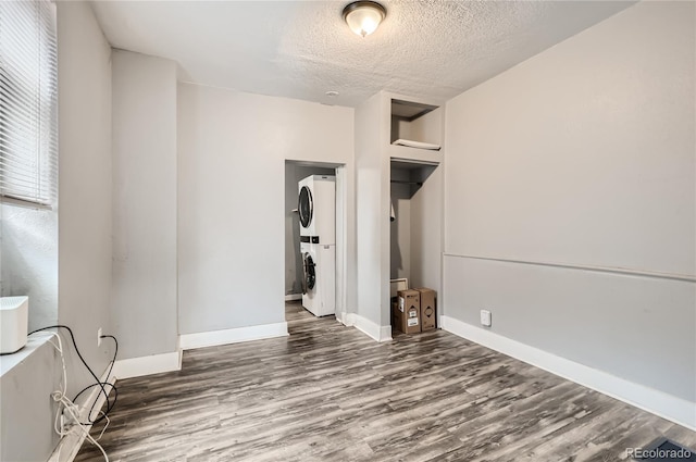 unfurnished bedroom featuring a textured ceiling, dark hardwood / wood-style floors, and stacked washer and clothes dryer