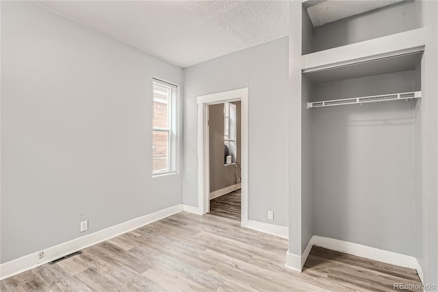 unfurnished bedroom featuring light wood-type flooring, a textured ceiling, and a closet