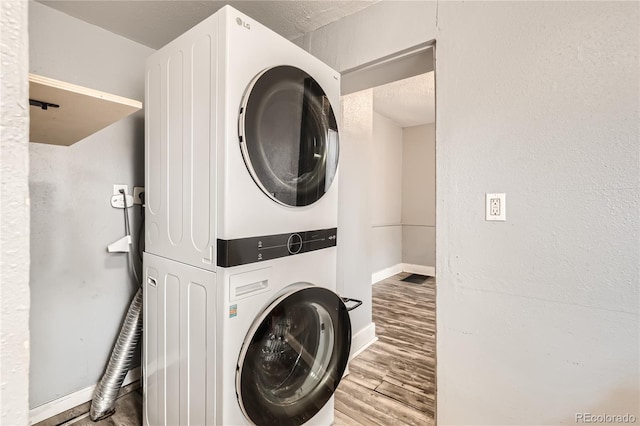 clothes washing area with hardwood / wood-style flooring and stacked washer and clothes dryer