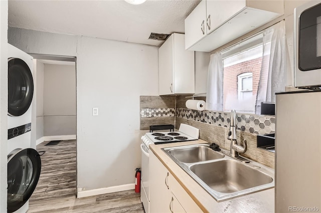 kitchen with sink, stacked washer and dryer, decorative backsplash, white cabinets, and light wood-type flooring