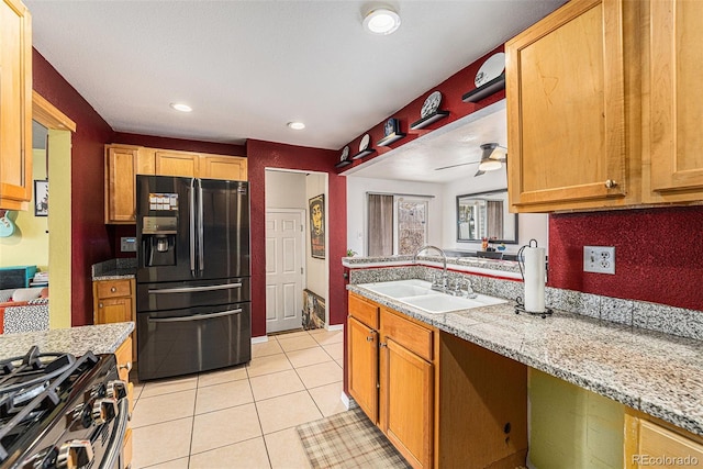 kitchen featuring light tile patterned flooring, a sink, a ceiling fan, black fridge, and stainless steel range with gas stovetop