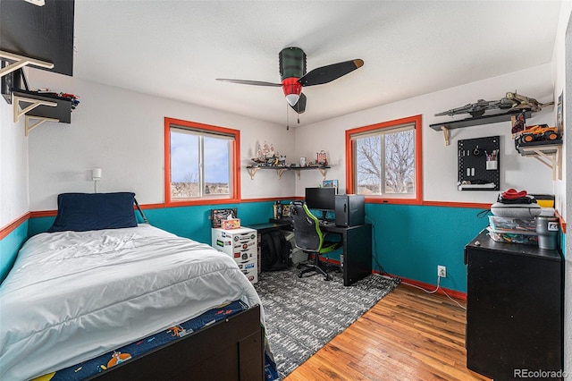 bedroom featuring ceiling fan, multiple windows, baseboards, and wood finished floors