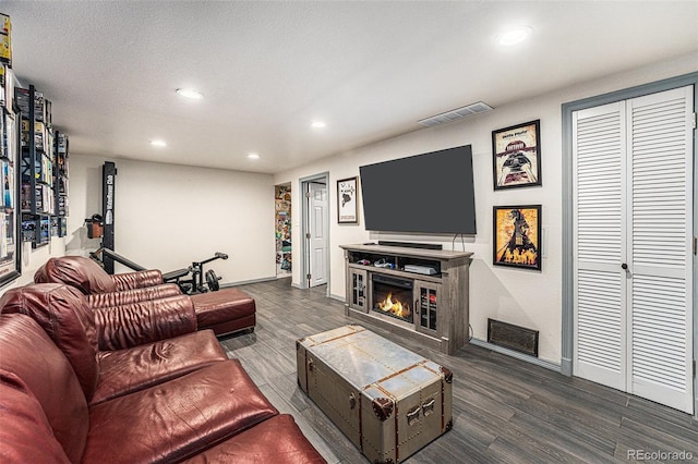 living area with wood finished floors, a glass covered fireplace, visible vents, and recessed lighting