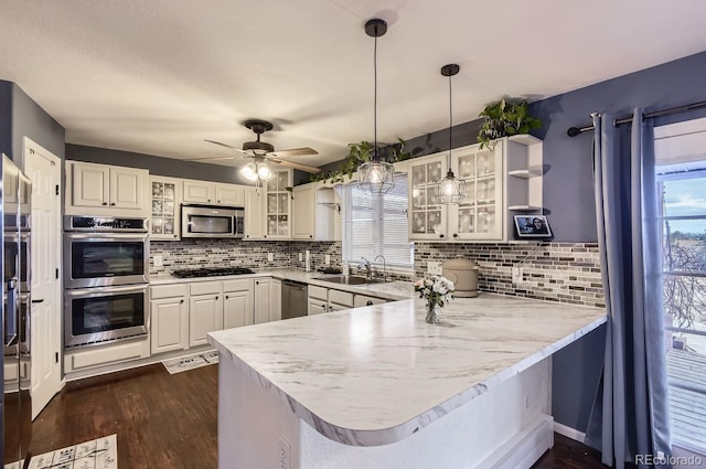 kitchen featuring appliances with stainless steel finishes, dark hardwood / wood-style floors, white cabinetry, hanging light fixtures, and kitchen peninsula