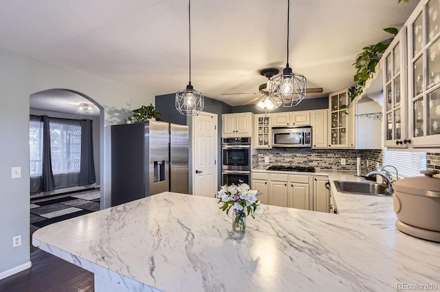 kitchen with sink, hanging light fixtures, stainless steel appliances, light stone counters, and decorative backsplash