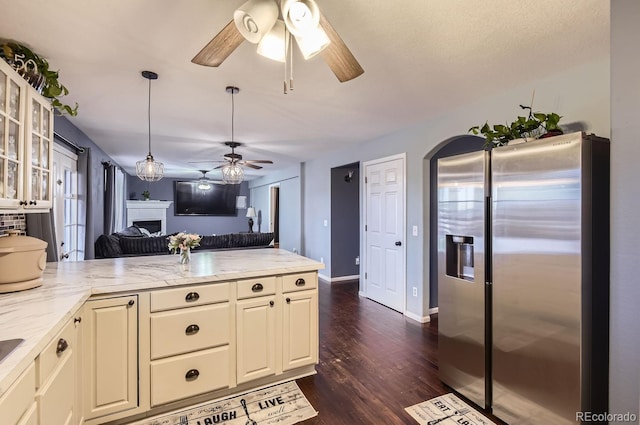 kitchen with pendant lighting, dark wood-type flooring, stainless steel fridge, ceiling fan, and light stone counters