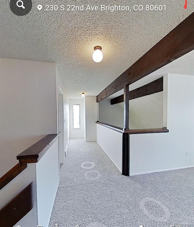 hallway featuring light colored carpet, beam ceiling, and a textured ceiling