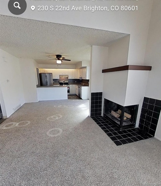 unfurnished living room featuring ceiling fan, a fireplace, a textured ceiling, and dark colored carpet