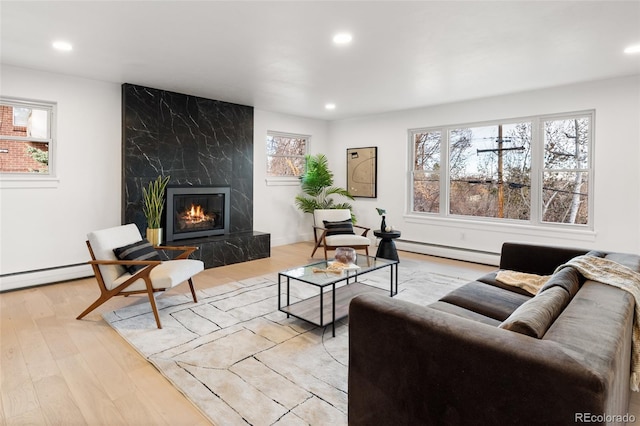 living room with a high end fireplace, light hardwood / wood-style floors, and baseboard heating