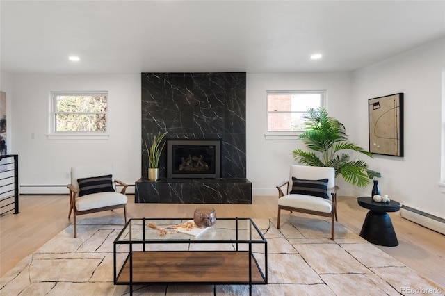 living room with baseboard heating, a premium fireplace, a healthy amount of sunlight, and light wood-type flooring