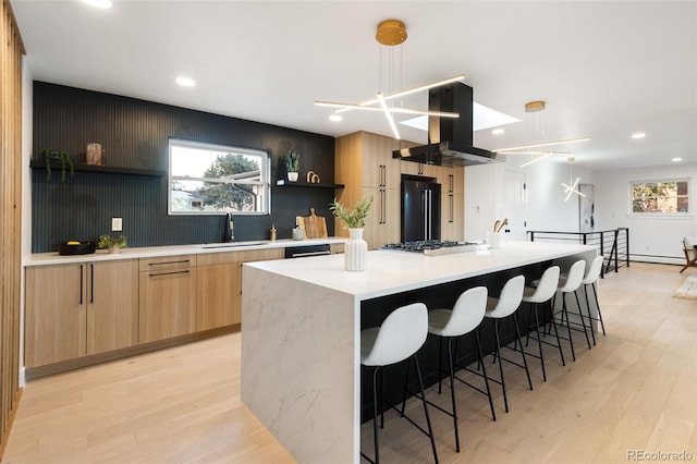 kitchen featuring island range hood, a spacious island, sink, pendant lighting, and light hardwood / wood-style floors