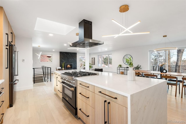 kitchen with light brown cabinets, decorative light fixtures, a large island, island range hood, and stainless steel appliances