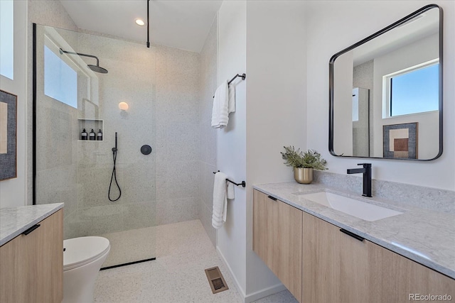 bathroom with toilet, a tile shower, and vanity