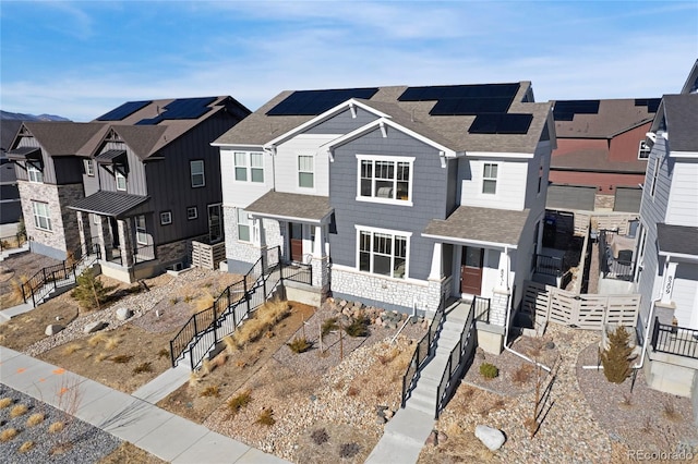 townhome / multi-family property with a shingled roof, a residential view, covered porch, fence, and roof mounted solar panels