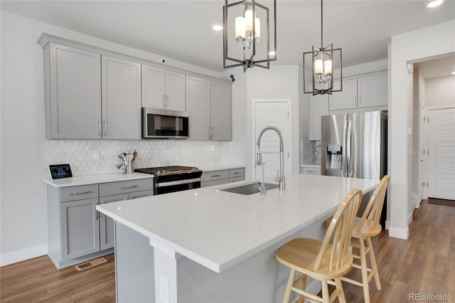 kitchen with appliances with stainless steel finishes, backsplash, a sink, and gray cabinetry