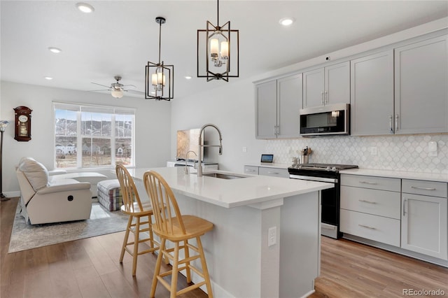 kitchen featuring a center island with sink, stainless steel appliances, gray cabinets, open floor plan, and a sink