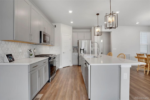 kitchen featuring appliances with stainless steel finishes, light wood-type flooring, a sink, and decorative backsplash