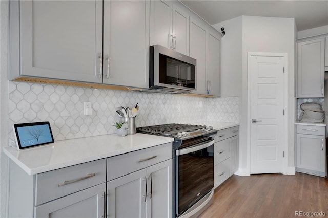 kitchen featuring decorative backsplash, appliances with stainless steel finishes, dark wood-type flooring, light countertops, and gray cabinetry