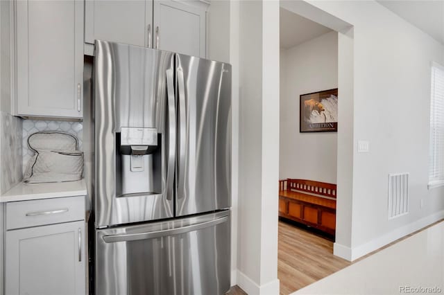 kitchen with visible vents, light wood-style floors, light countertops, decorative backsplash, and stainless steel fridge