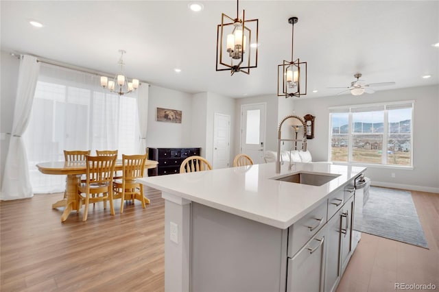 kitchen featuring light countertops, light wood-style flooring, open floor plan, a kitchen island with sink, and a sink