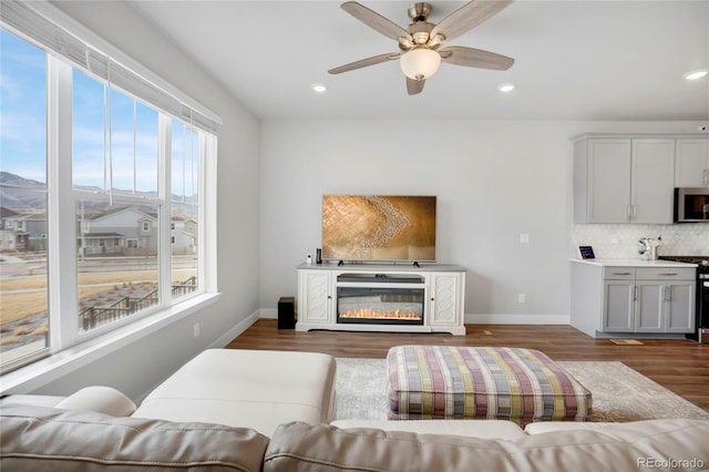 living area with dark wood-style flooring, recessed lighting, a ceiling fan, a glass covered fireplace, and baseboards